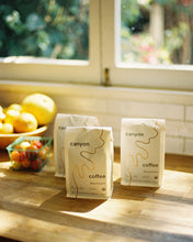 Load image into Gallery viewer, three basgs of Beachwood USDA organic coffee by Canyon Coffee in the kitchen with a bowl of fruit
