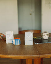 Load image into Gallery viewer, A bag of Afternoon Decaf Coffee by Canyon Coffee at home with ceramic mugs on a wood dining table
