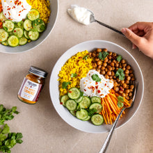 Load image into Gallery viewer, Bowl of salad with chickpeas, carrots, and cucumbers on a beige surface with a jar New Harvest Turmeric from Burlap & Barrel