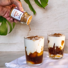 Load image into Gallery viewer, Hand pouring a jar of Royal Cinnamon into two glasses of iced coffee from Burlap & Barrel