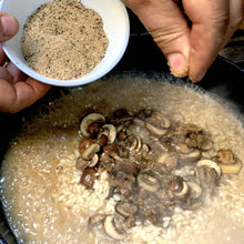 Load image into Gallery viewer, cooking risotto with mushrooms and a hand sprinkling with omnivore Porcini