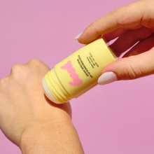 Load image into Gallery viewer, Hand applying a yellow stick of sunscreen with a pink logo on a pink background