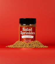 Load image into Gallery viewer, A bottle of Chili Crisp SaladSprinkles nestled in a little pile of salad sprinkles on a red background.