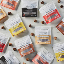 Load image into Gallery viewer, AMG Snack bags in every flavor on marble with energy bites scattered.