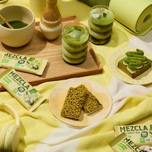 Load image into Gallery viewer, Matcha-themed spread with MEZCLA crispy bars, green tea drinks, desserts and yoga mat on yellow patterned fabric