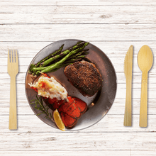 Load image into Gallery viewer, An elegant dinner setting featuring Holy City Straw Co. brand eco-friendly wooden cutlery, with a fork to the left and knife and spoon to the right. The meal includes a well-seasoned steak, succulent lobster tail, a scoop of creamy crab meat, and a side of grilled asparagus, all artistically arranged on a round plate with a rustic wooden table background
