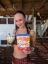 Load image into Gallery viewer, Photo of our friend holding a bag of mini stroopwafels in tropical surroundings.
