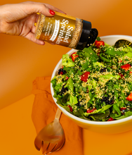 Load image into Gallery viewer, An image of a hand holding a bottle of Maple Sea Salt SaladSprinkles, sprinkling them over a delicious green salad. 
