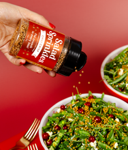 Load image into Gallery viewer, An image of a hand holding a bottle of Chili Crisp SaladSprinkles, sprinkling them over a delicious green salad. 
