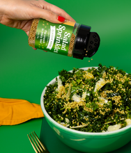 Load image into Gallery viewer, An image of a hand holding a bottle of Classic Herb SaladSprinkles, sprinkling them over a delicious green salad. 
