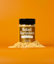 Load image into Gallery viewer, A bottle of Maple Sea Salt SaladSprinkles nestled in a little pile of salad sprinkles on an orange background.
