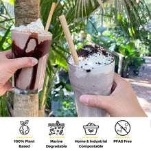 Load image into Gallery viewer, Two hands are holding iced frappuccino drinks in clear glasses, one decorated with chocolate drizzle and whipped cream, and the other topped with whipped cream and cookie crumbles. Each drink features a biodegradable straw made from reed stems. The background is lush greenery, suggesting an outdoor setting. Below the image, four icons emphasize the eco-friendly nature of the straws, describing them as 100% plant-based, marine degradable, home and industrial compostable, and PFAS-free.
