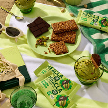Load image into Gallery viewer, Green MEZCLA crispy bars with rice and chocolate displayed on lime green plate alongside dark chocolate squares, pistachios, and green ice cream in glass bowls on striped towel
