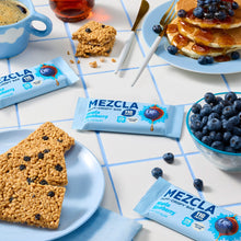 Load image into Gallery viewer, MEZCLA puff-crispy bars in maple blueberry flavor arranged on white tiled surface with fresh blueberries, pancakes, coffee, and granola bars
