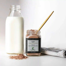Load image into Gallery viewer, Open glass jar of Vanilla Hot Cocoa Mix next to a scatter of the mix, a jug of milk, and a towel.
