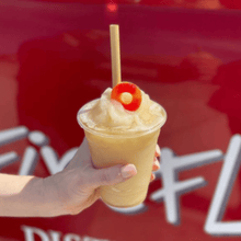 Load image into Gallery viewer, hand holding sour peach frozen cocktail with reed drinking straw
